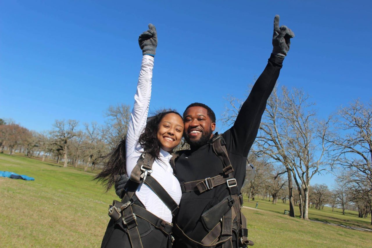 Couple stands together with hands pointed towards the sky after an awesome skydive at the skydiving company in texas