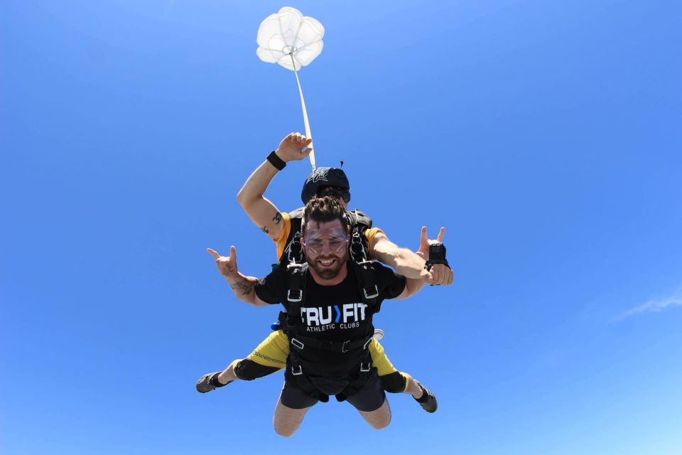 Man wearing a true fit shirt smiles during free fall portion of his skydive