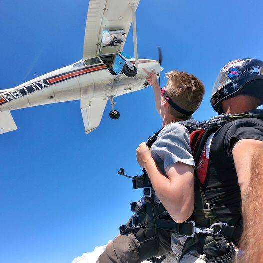 Man wearing white shirt and dark skydiving googles smiles while enjoying his tandem skydive at the skydiving company in texas