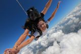 Women wearing white shirt smiles and touches hand with a fellow skydiver during free fall