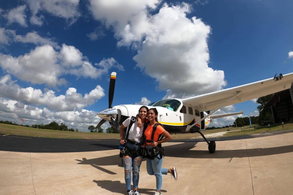 Two females hugging in front of the skydiving company aircraft