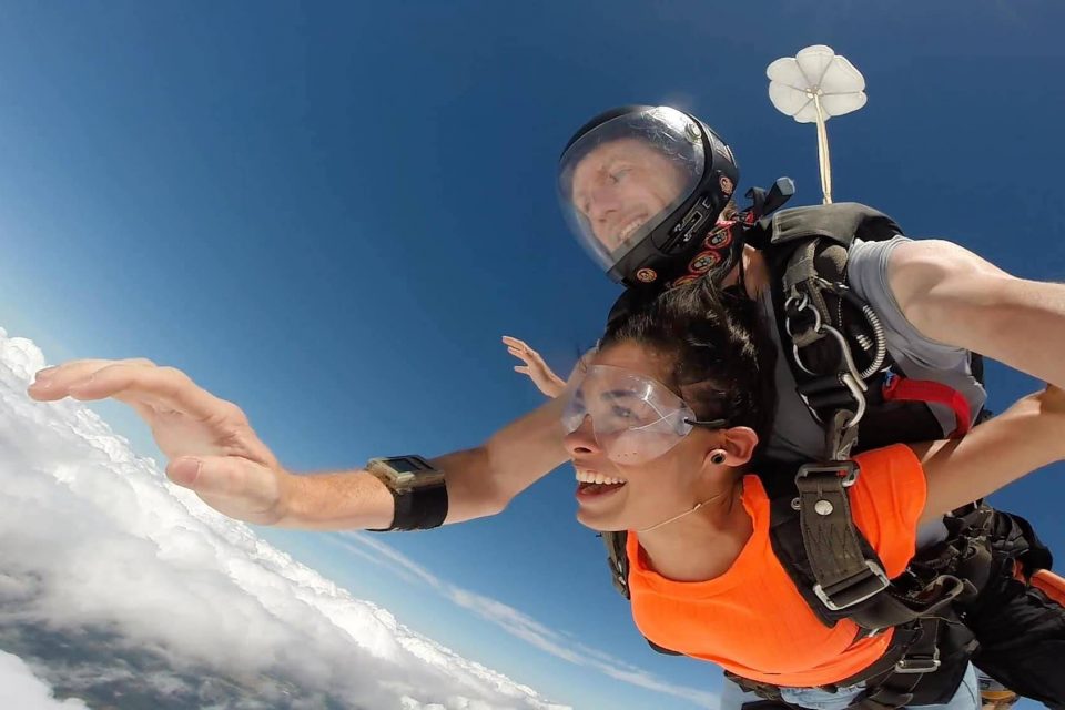 Women wearing an orange shirt and clear skydiving googles enjoys free fall with a The Skydiving Company tandem instructor