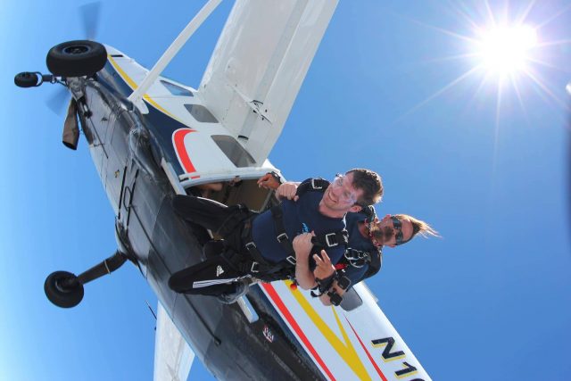 Man in blue shirt takes the jump for a the skydiving company aircraft into free fall on a beautiful sunny day