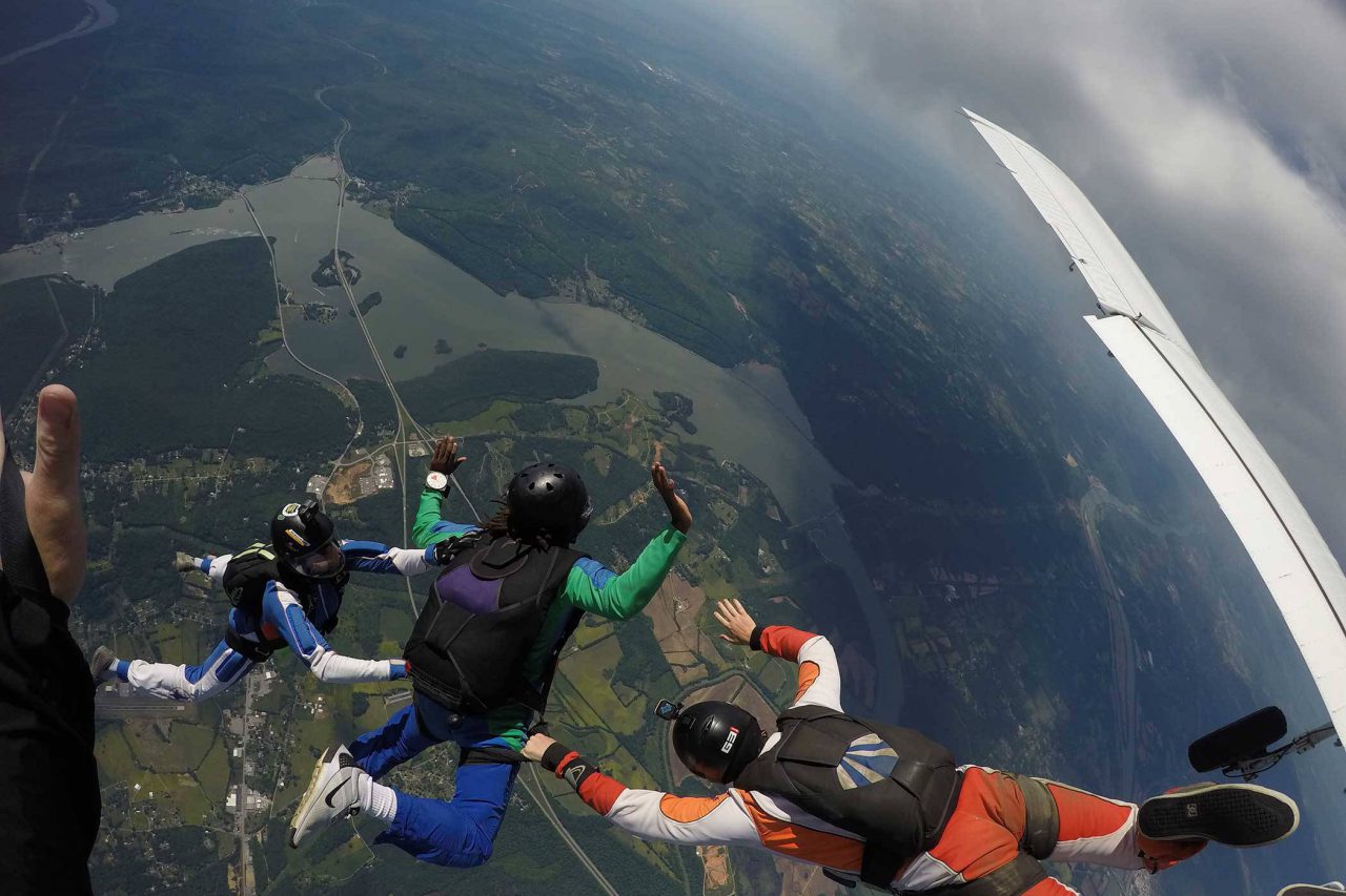 AFF student wearing green and blue skydiving gear practices the free fall portion of his skydive with instructors