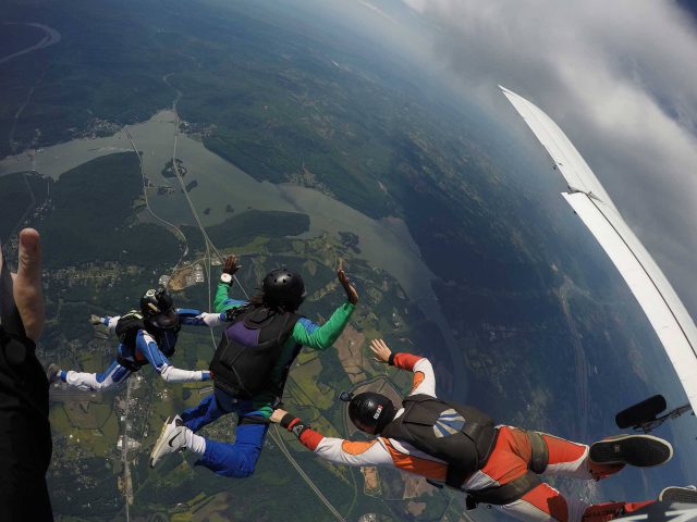 AFF student wearing green and blue skydiving gear practices the free fall portion of his skydive with instructors