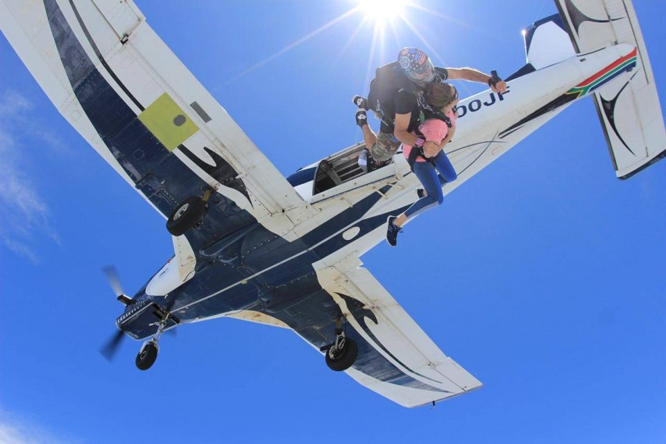 Female tandem skydiver wearing pink shirt jumps from airplane into free fall