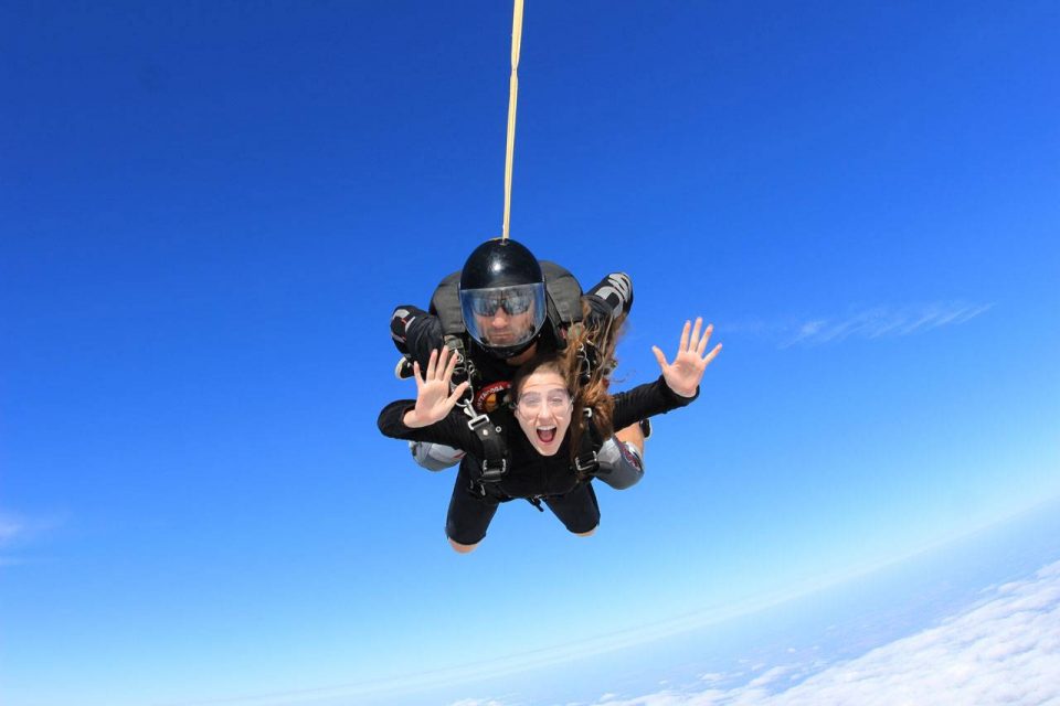 Women in black shirt smiles with arms out during an amazing skydive at the skydiving company